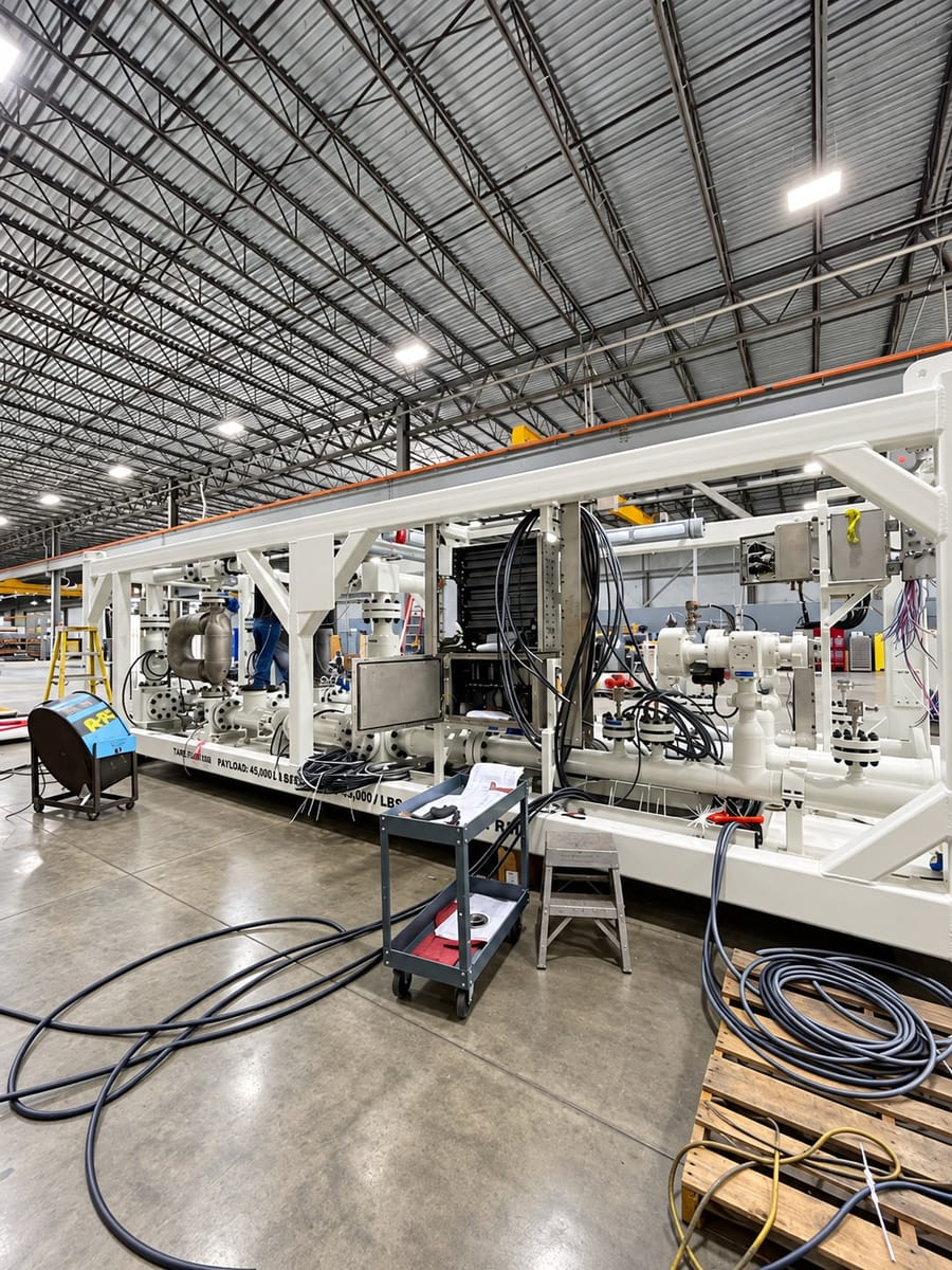 A long skid-mounted process package under build: valves, instrument enclosures and piping set along the frame, cabling run out across the floor.