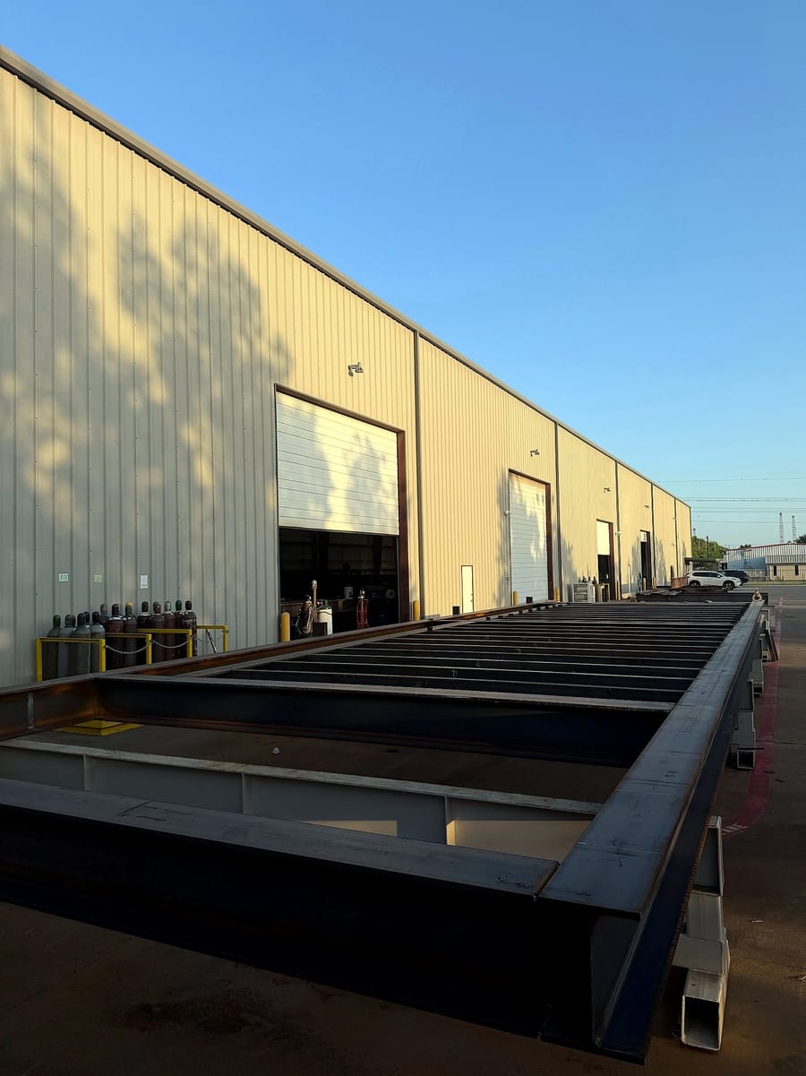 A long fabricated steel frame staged in the yard outside the shop.