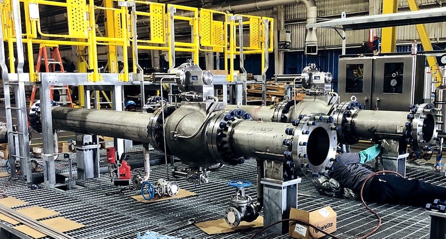 A long valve and piping assembly set up on a raised platform for assembly work.