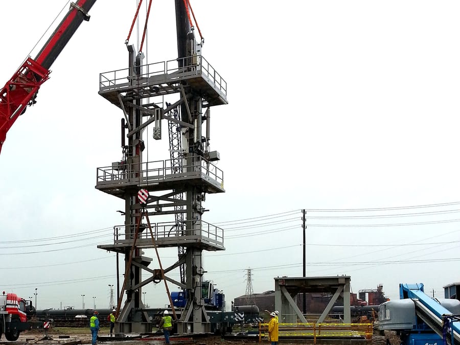 A multi-level structural tower held on the crane during erection at site, the crew working at the base.
