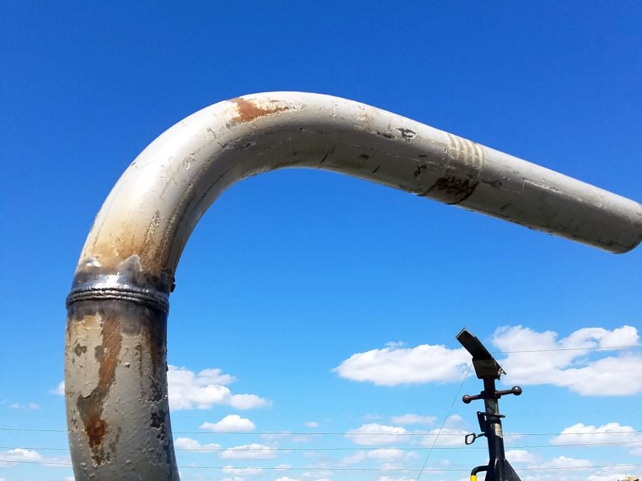 A completed field weld on a large pipe bend rising from the equipment deck against open sky.