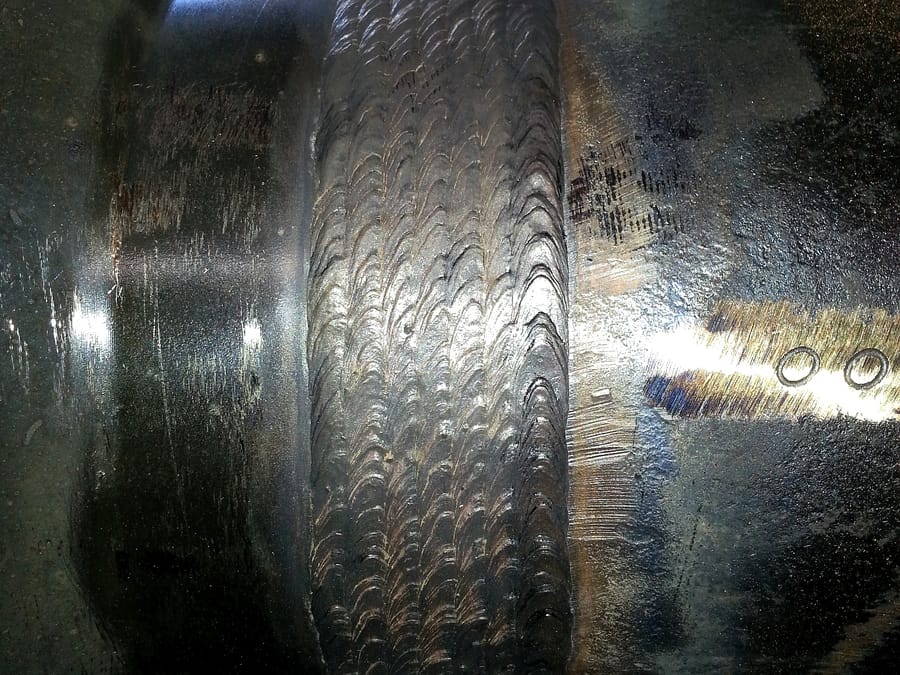 A close view of a weld overlay band on a shaft, each bead overlapping the last, machined surfaces either side.