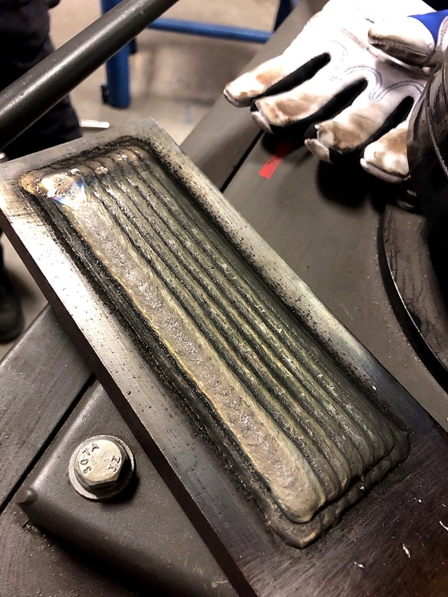 A weld overlay test coupon, parallel beads laid across the plate.