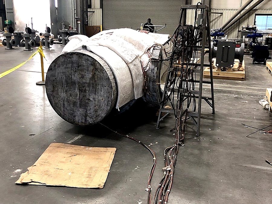 A large body wrapped in heat treatment insulation, thermocouple leads gathered and run back across the floor.