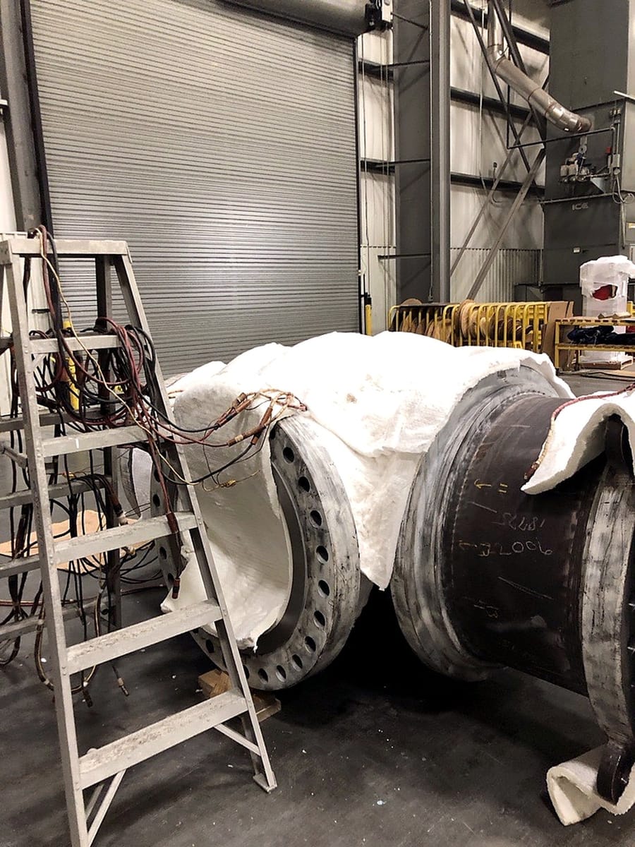 A heavy flanged body under insulation blankets during heat treatment.
