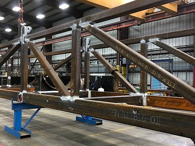 A welded structural truss on stands under the shop crane, gussets and lifting lugs complete.
