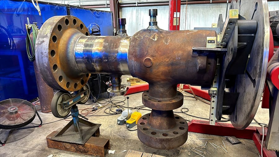 A valve body and flanged spool set up on the welding rig.