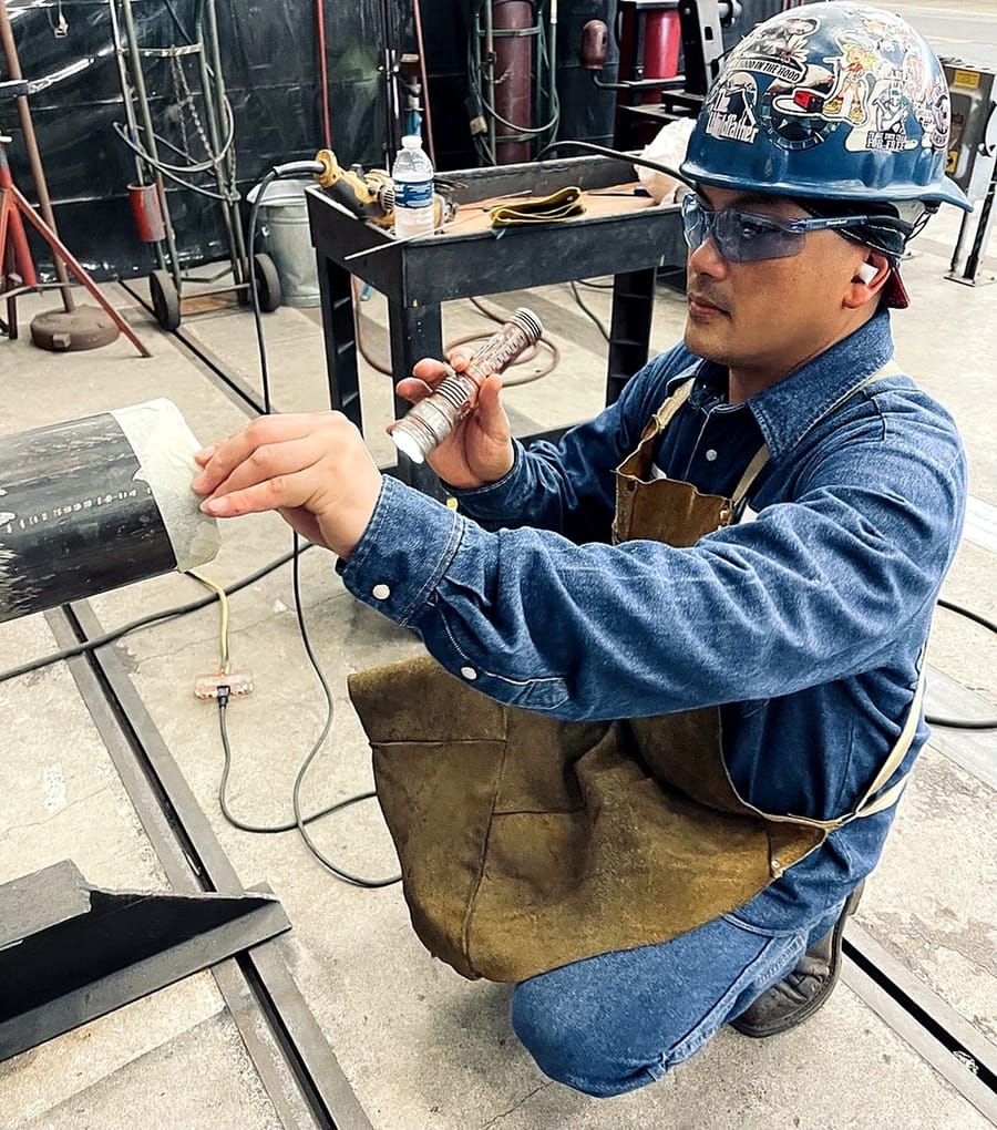 A technician applying developer during a dye penetrant examination of a weld.
